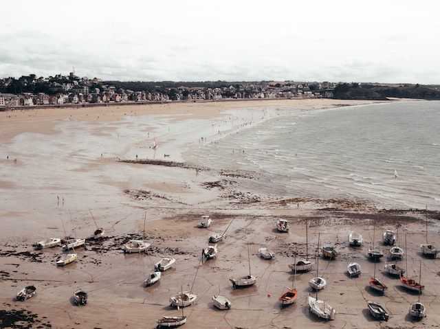 Vue d'une plage à marée basse avec plusieurs bateaux couchés sur le sable. 