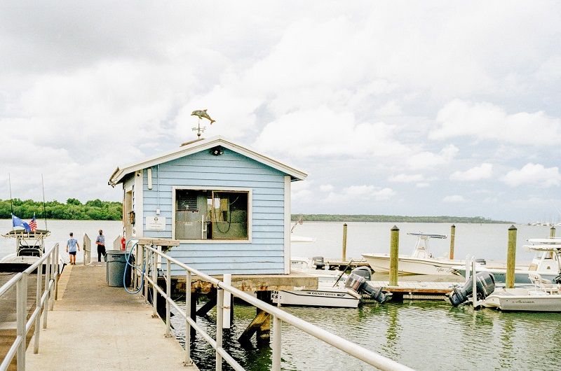 Une petite maison bleue en bois sur une jetée avec une poignée de bateaux amarrés.