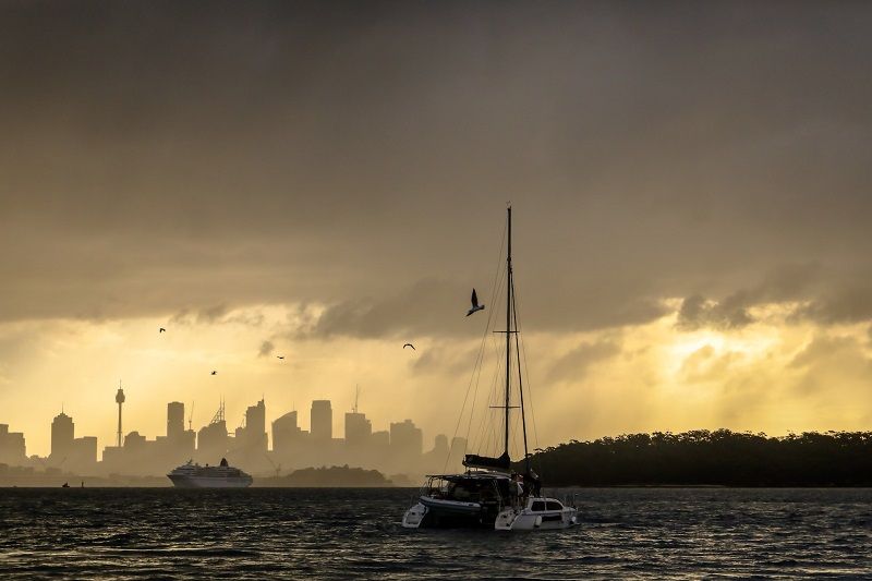 Catamaran à voile au large de la côte de Sydney avec des nuages de pluie.
