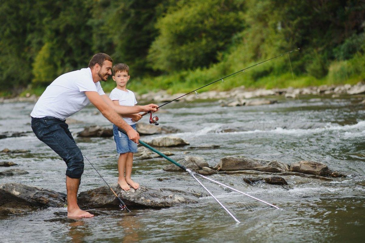 Enfants concentrés lors d'une leçon de pêche encadrée par un guide expérimenté au bord de la rivière en été.