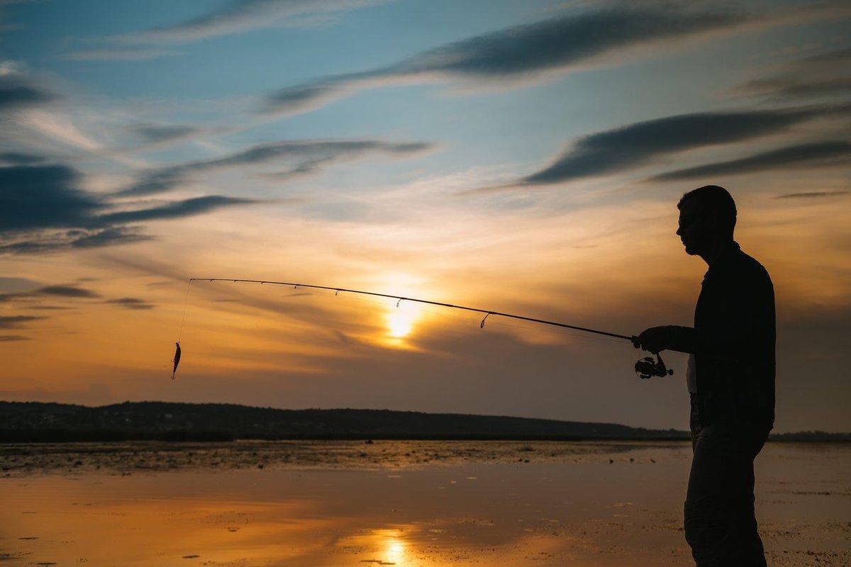 Fisherman casting lure at sunset near a sandy beach, idéale pour la pêche en mer en été sur la côte française.