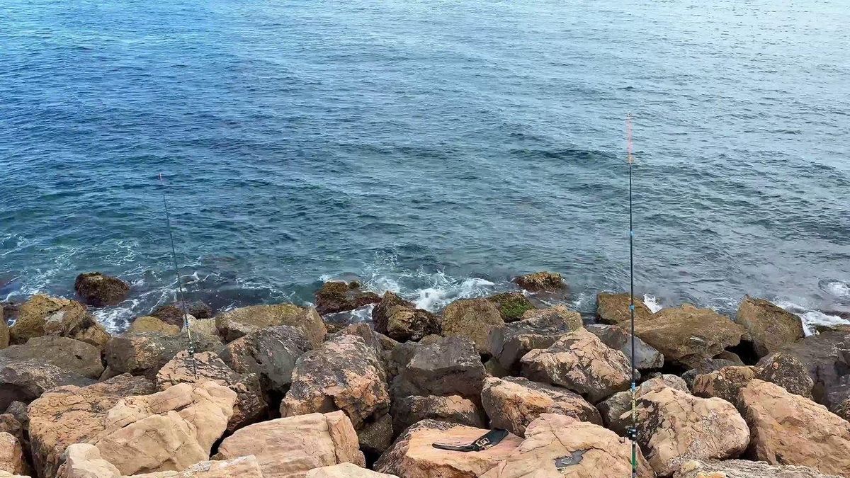 Fisherman rocky coast sea fishing : un pêcheur en mer lançant sa ligne face à une mer agitée et un ciel clair.