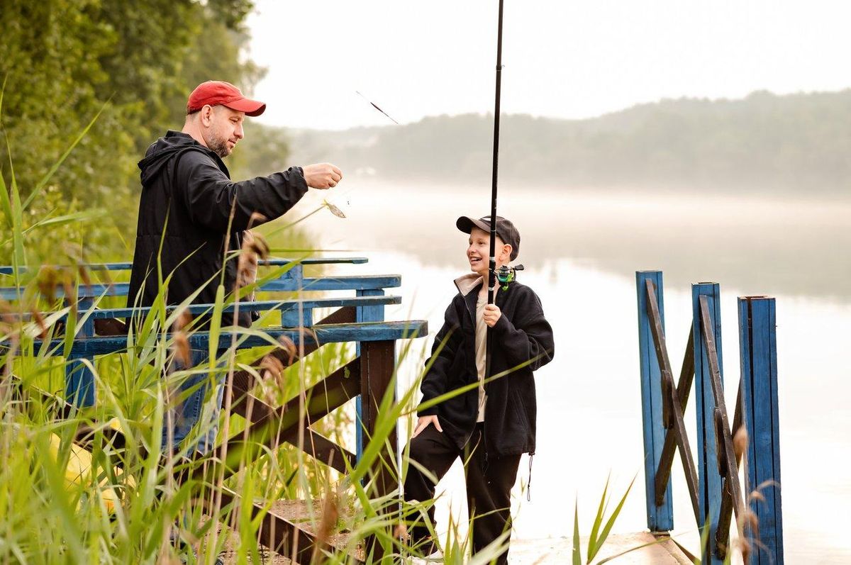 Groupe familial pêchant au bord d’un étang calme, enfants utilisant des cannes légères avec flotteurs colorés.