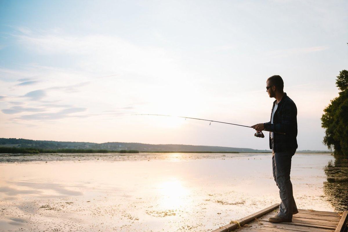 Jeune pêcheur pratiquant la pêche durable au printemps au lever du soleil sur un lac paisible.