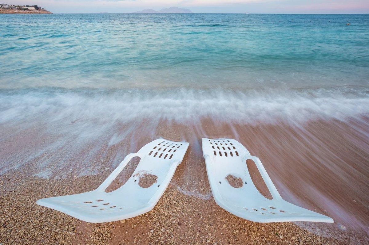 Personne en fauteuil roulant utilisant un fauteuil amphibie sur une plage accessible, facilitant la pratique des sports nautiques.