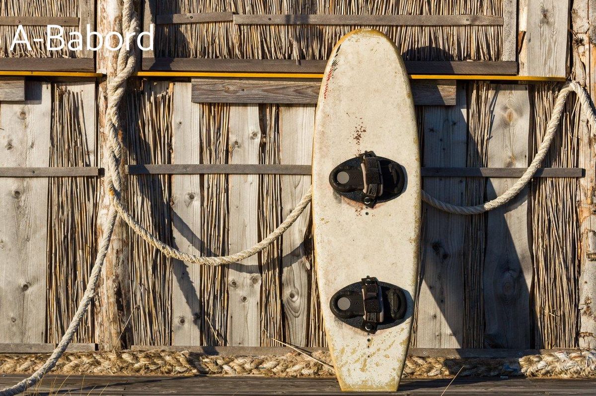 Planche usée appuyée sur cabane en bois : votre premier pas vers le surf foil.
