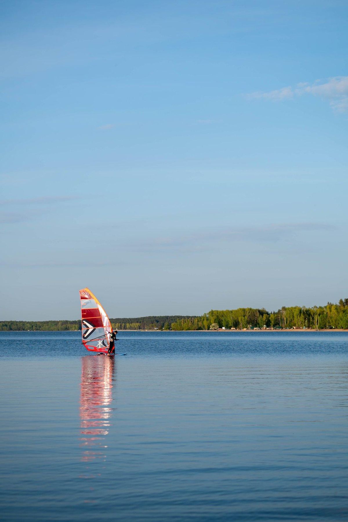 Pratiquant débutant en windsurf sur eau calme avec une planche volumineuse sous un vent modéré.