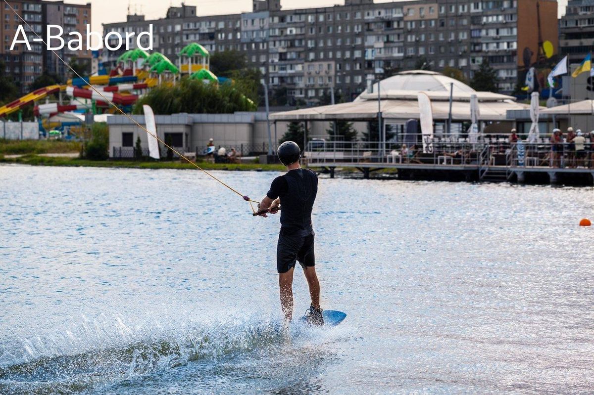 Séance de wakeboard initiation : un homme en combinaison et casque en équilibre sur la planche.