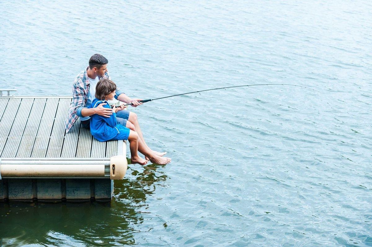 Un enfant tenant une canne à pêche légère sur un ponton, avec un parent montrant fièrement une prise.