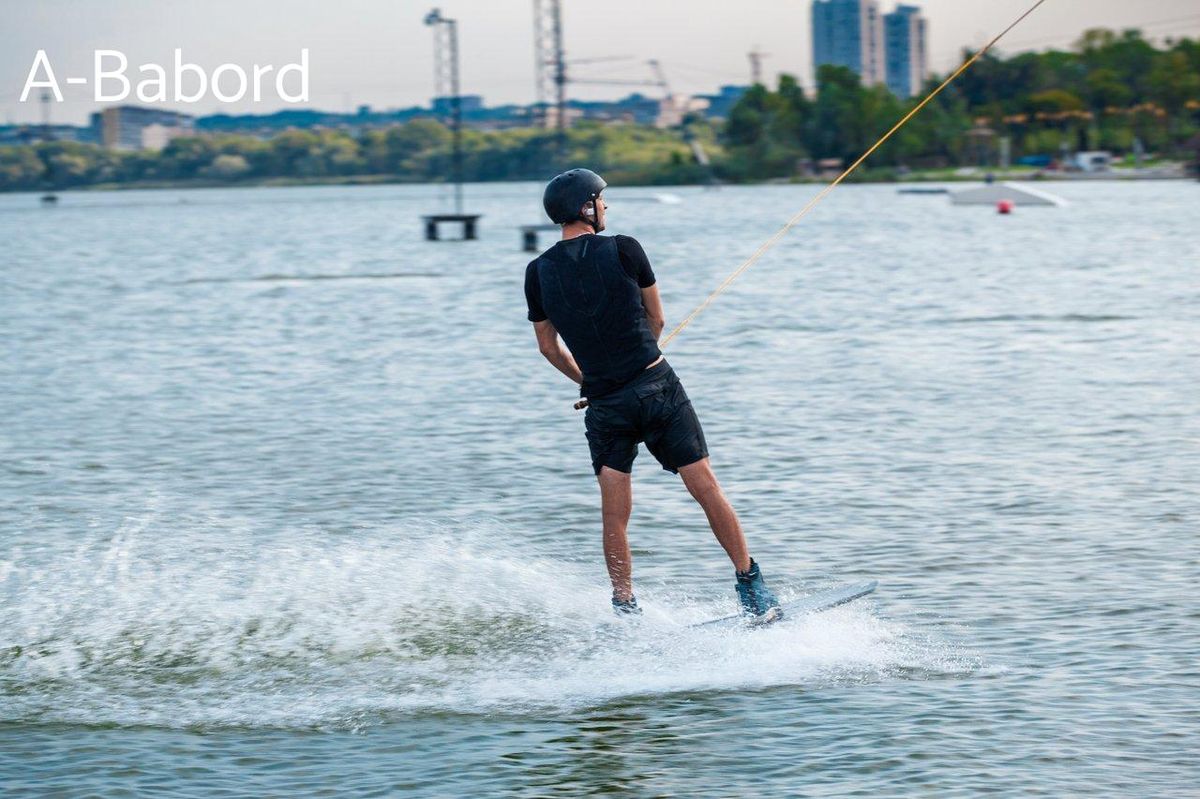 Un wakeboarder débutant glisse sur l'eau d'une rivière urbaine, apprenant les bases du wakeboard.