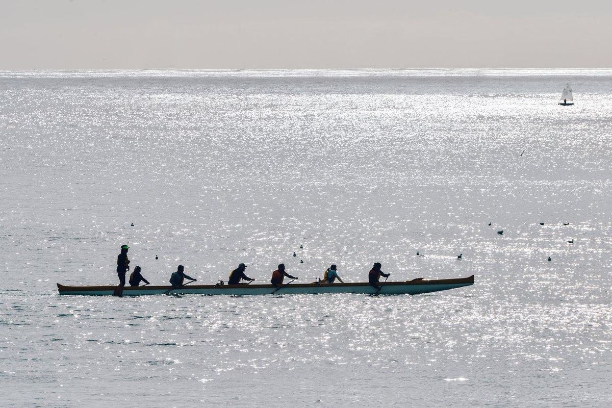 Une compétition de va’a polynésien en pleine course synchronisée sur le lagon au coucher du soleil.