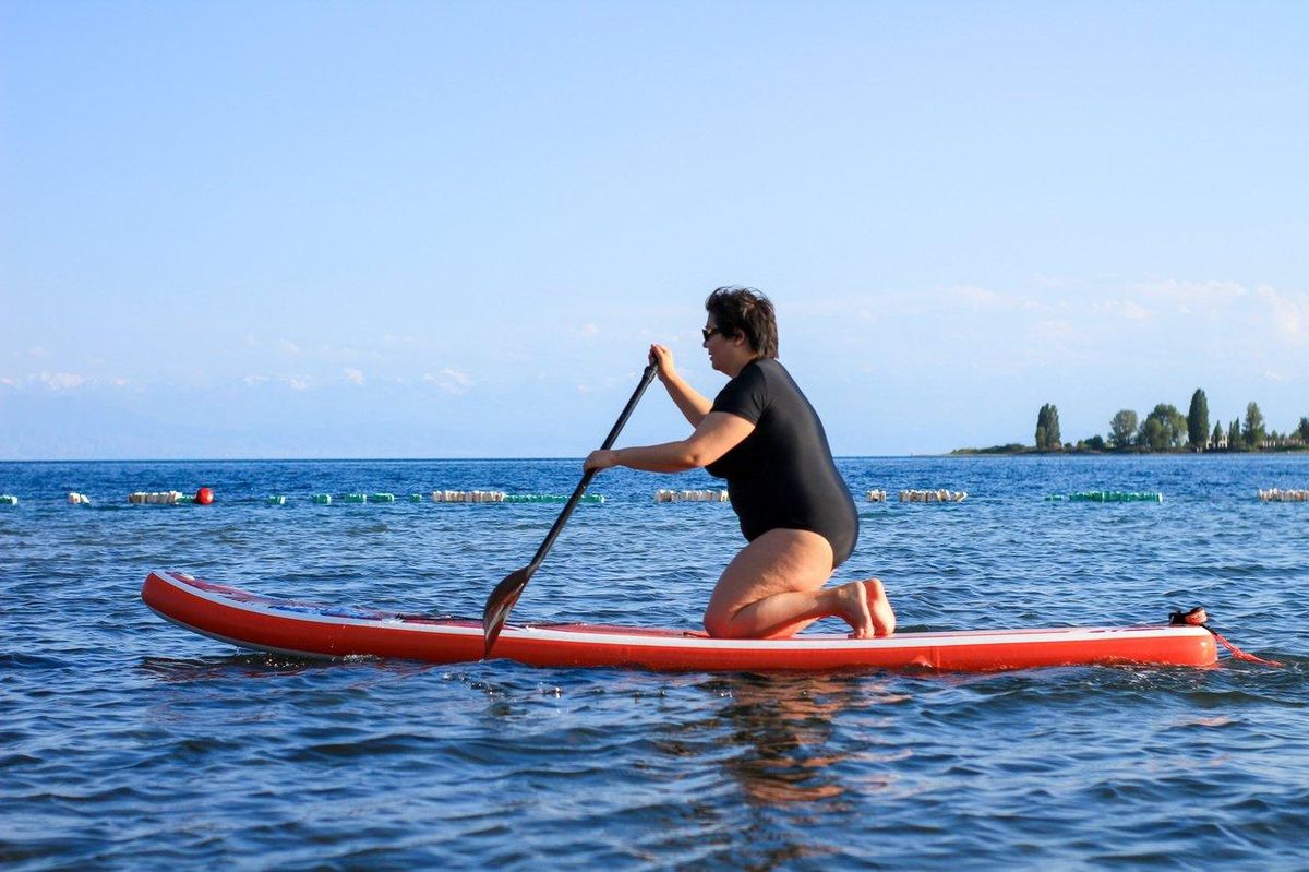 Une débutante en stand up paddle sur une planche orange gonflable, naviguant calmement sur l'eau.