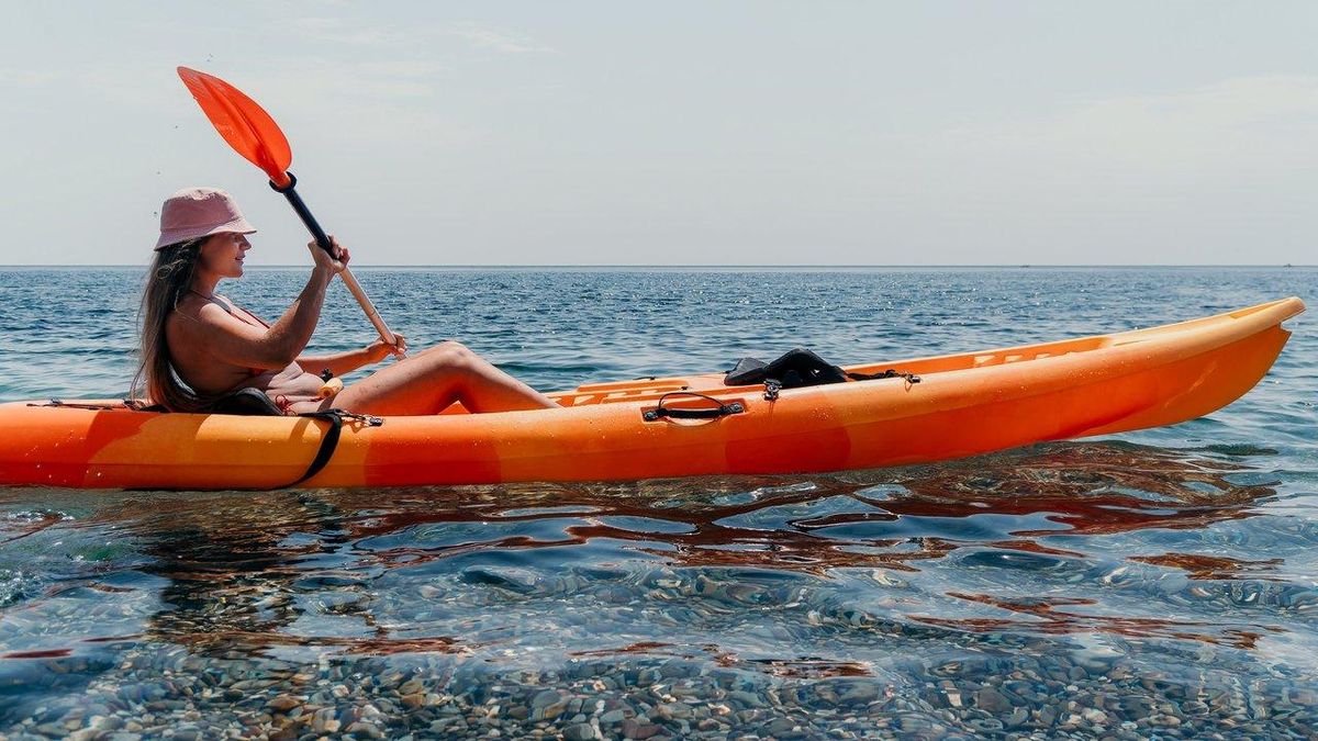 Une femme souriante navigue en rigide fishing kayak coastal, idéal pour la pêche en milieu côtier.