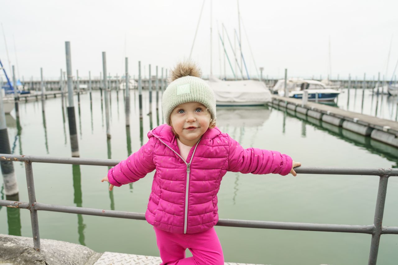Enfant portant un gilet de flottabilité néoprène au bord d’un ponton, près de la marina.