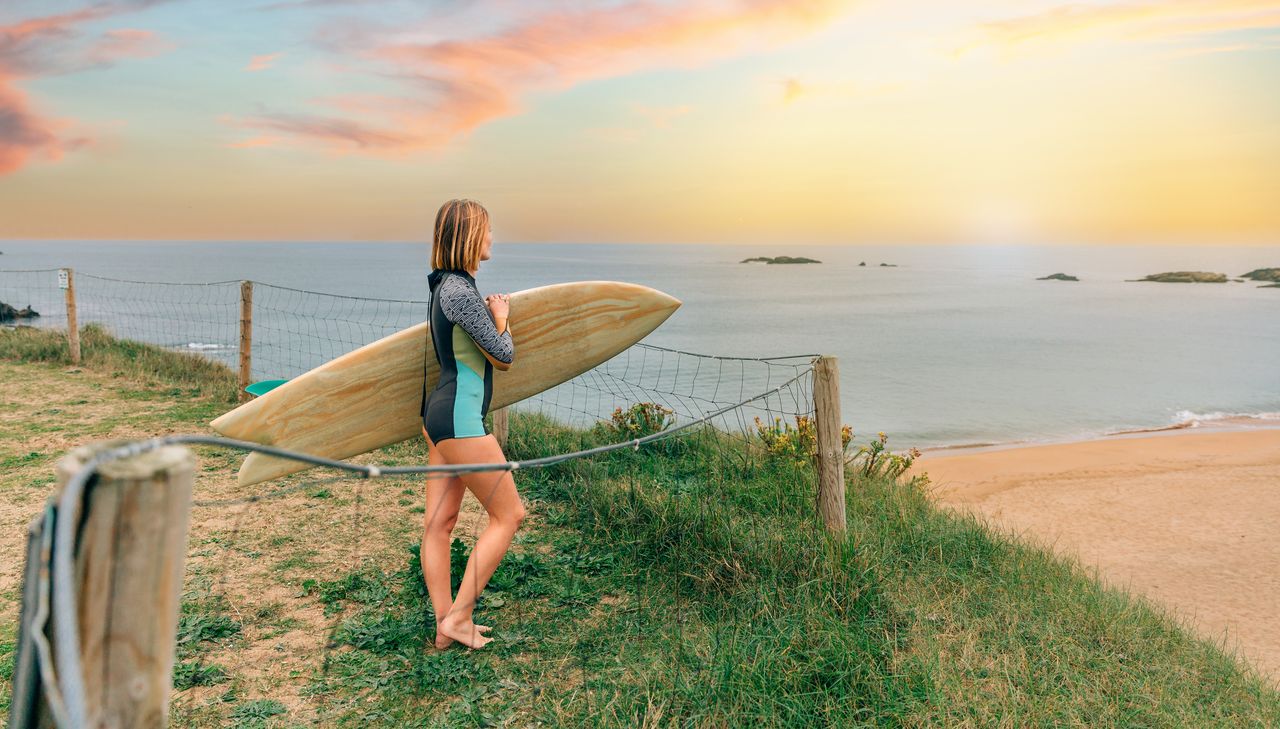 Jeune surfeuse débutante en combinaison avec planche de surf sur une plage européenne au coucher du soleil