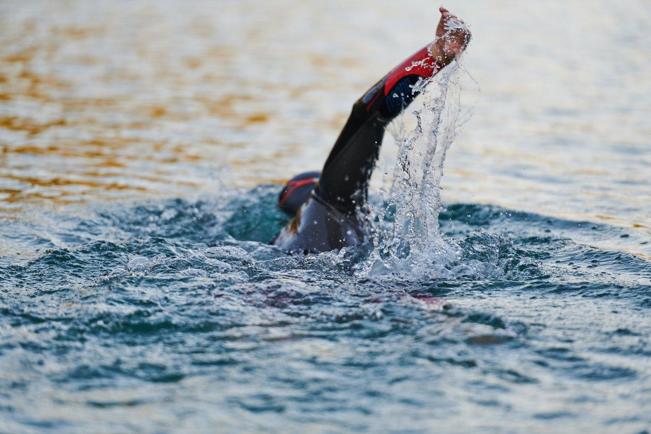 Nageurs en eau libre lors d’un open water triathlon, encadrés par des arbitres au lever du soleil.