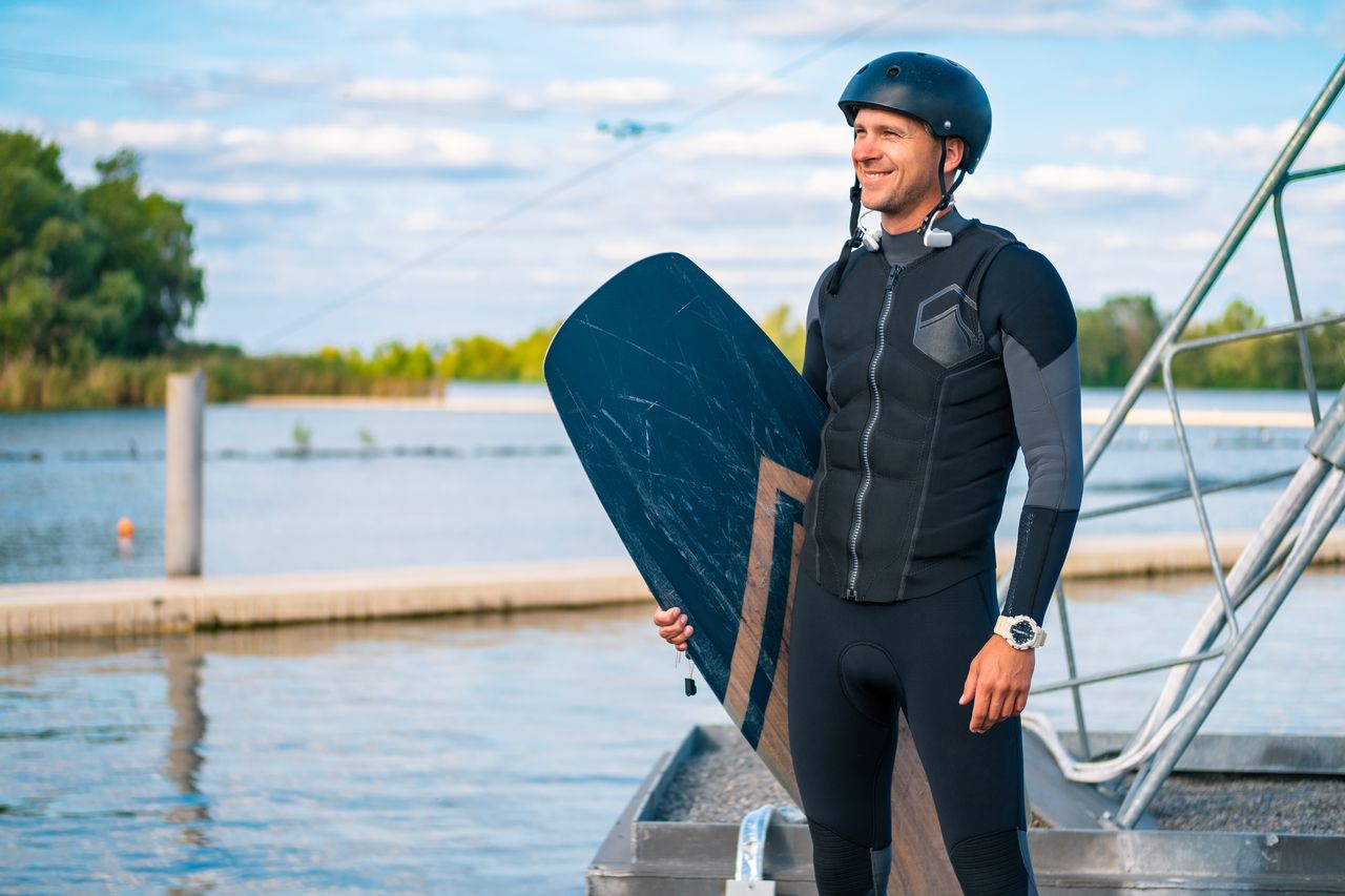 Pack wakeboard débutant avec planche et chausses sur fond de ponton en bois.