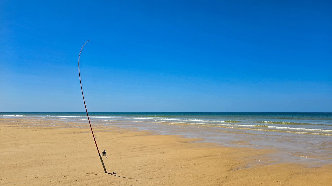 Pêcheur au bord d’une digue, canne légère et flotteur visible sur une mer calme.