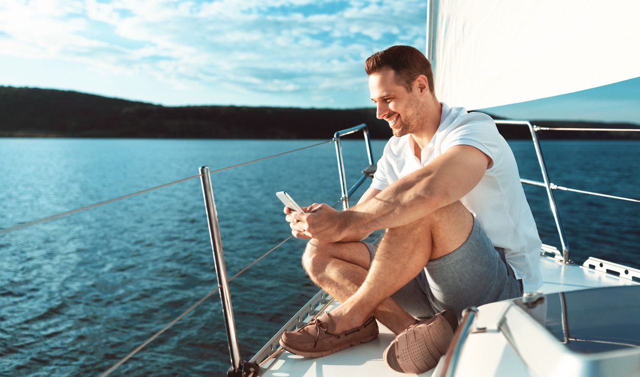 Pêcheur de loisir en mer consultant une application sur smartphone à bord d’un bateau.
