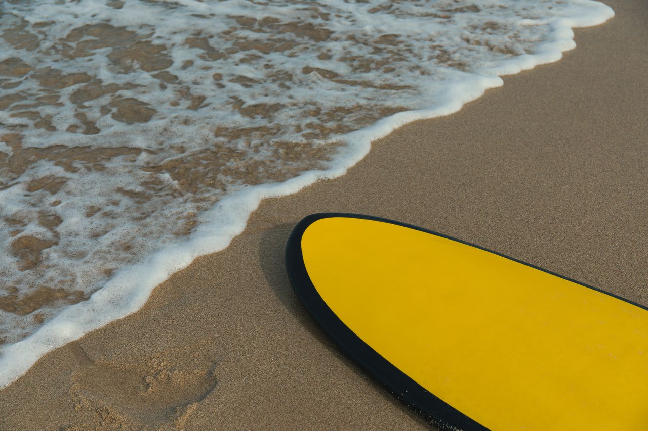 Quatre planches de surf Helm Supplies alignées sur le sable, avec de petites vagues en arrière-plan.