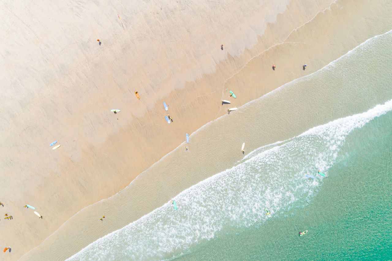 Surfeur réalisant un étirement des épaules sur la plage, en plan large pédagogique au lever du jour.