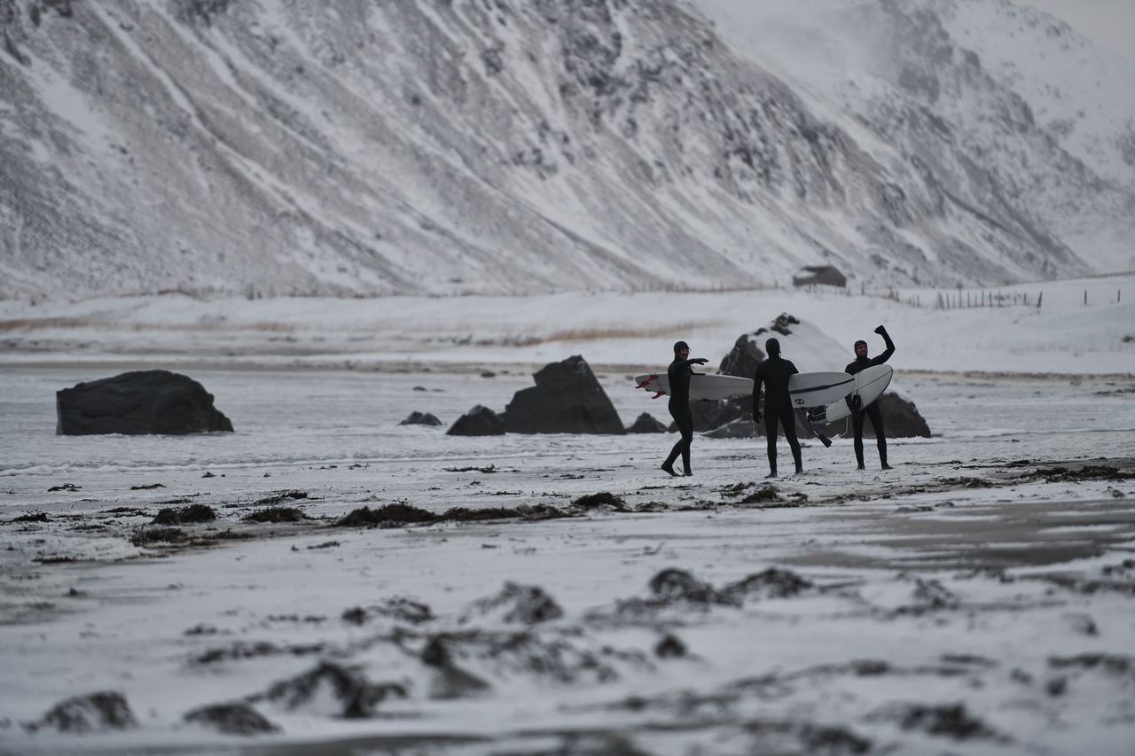 Surfeurs en combinaison épaisse sur une plage norvégienne, affrontant une houle hivernale spectaculaire.