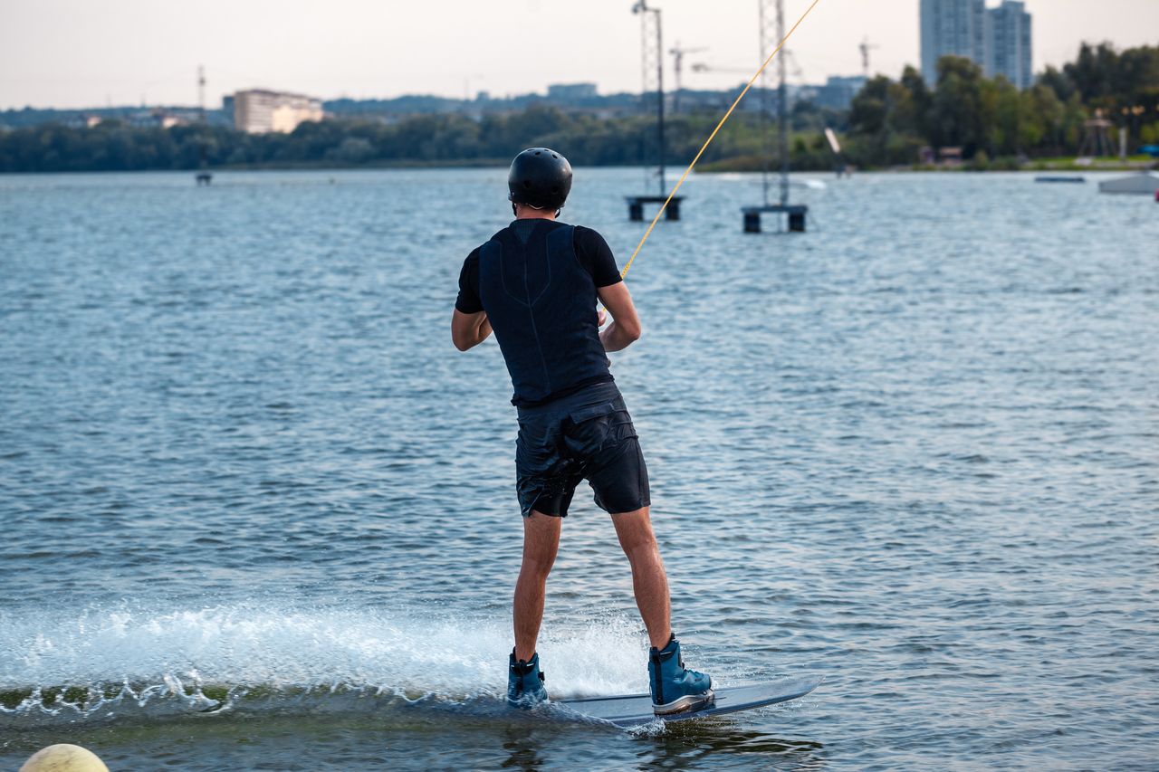 Wakeboardeur en combinaison néoprène 5/4 mm glissant sur plan d’eau froid sous lumière hivernale.